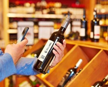 Uomo che scansiona con uno smartphone il codice QR su una bottiglia di vino - Eu-Label.info